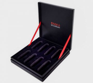 Black higed rigid presentation box with red ribbon stop and eva insert that says guerlain