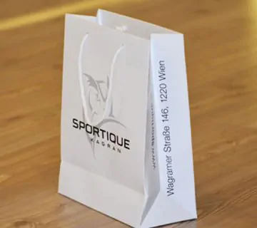 White unlaminated paper bag with white rope taht says sportique