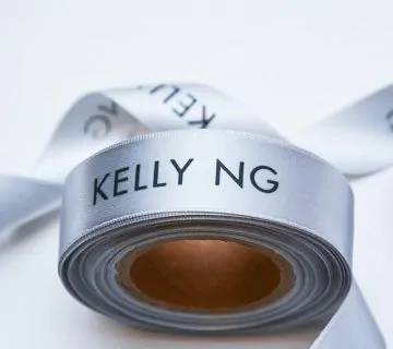 Logo printed silver satin ribbon roll that says Kelly NG