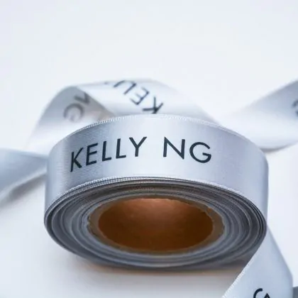 Logo printed silver satin ribbon roll that says Kelly NG