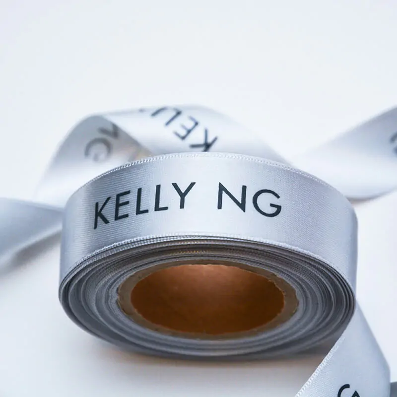 Logo printed silver satin ribbon roll that says Kelly NG